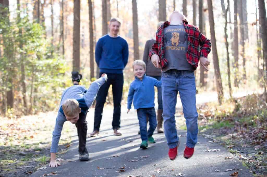 a family does a silly walk down a wooded path, the daughter's shirt says, "celebrate diversity"