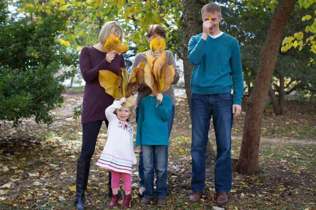 a family hides their faces with giant leaves while the girl in a dress peeks out