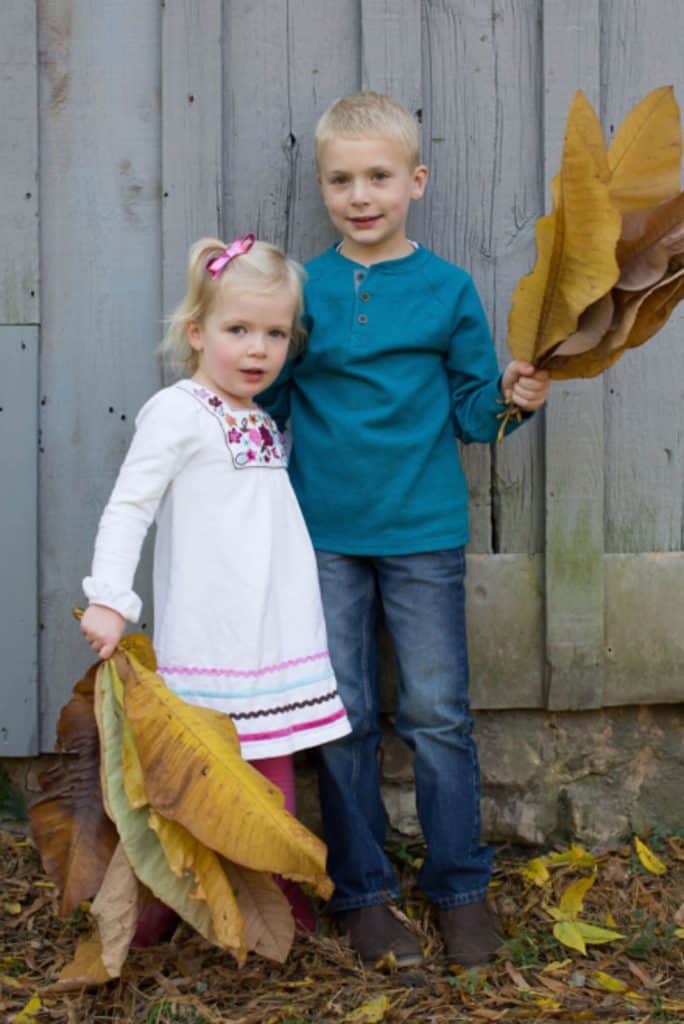 a brother and sister pose with giant leaves next to a barn