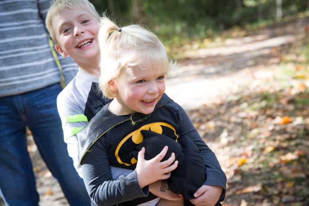a boy hugs his sister who is wearing a Batman costume