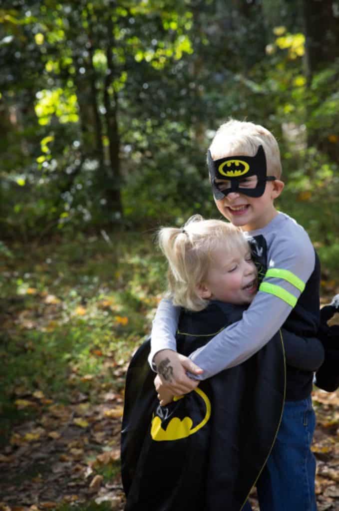 a sister hugs her brother wearing a Batman cape and he hugs her back, wearing her Batman mask.