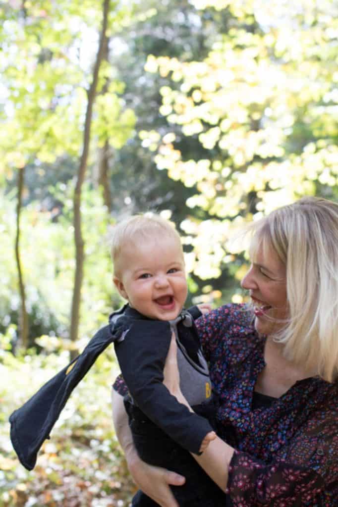a mom swings her baby boy who is wearing a Batman costume and laughing