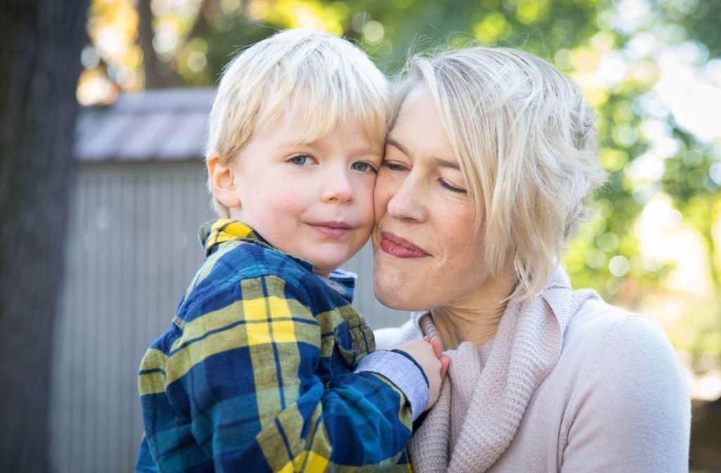 a mom cuddles her daughter who is wearing a flannel shirt and her hair is cut short