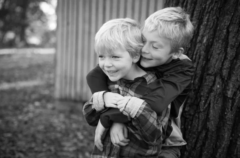 a brother hugs his sister who is wearing a falnnel shirt with her hair cut short