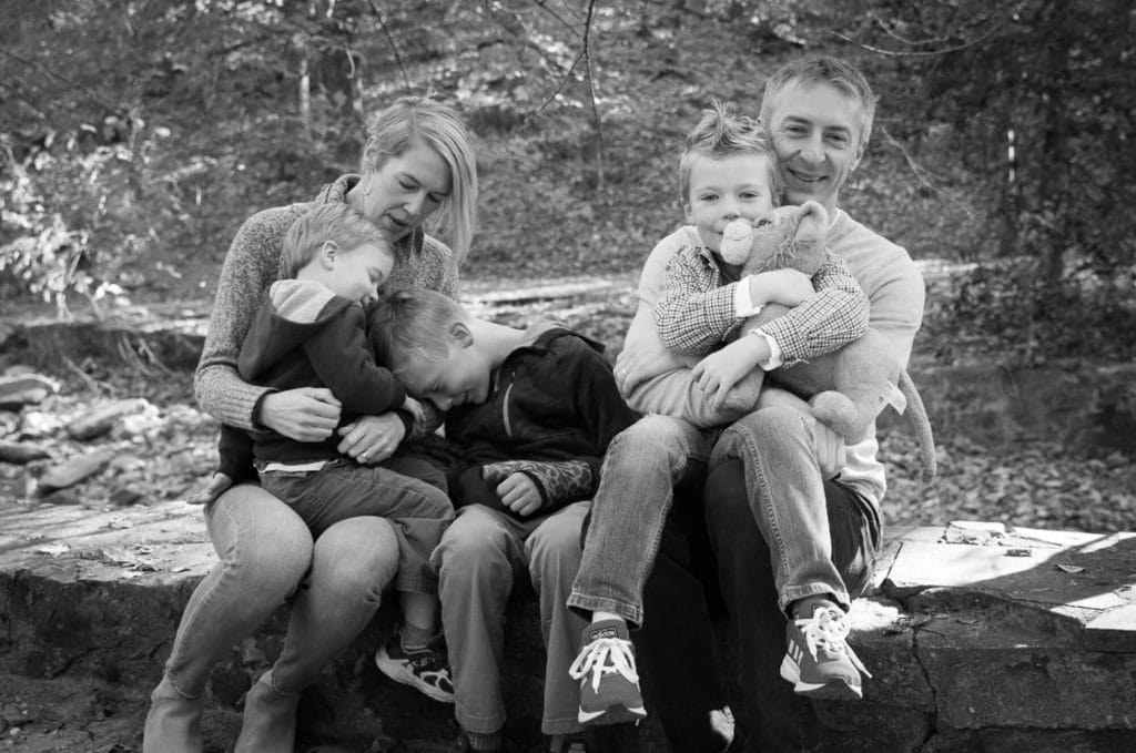 a family snuggles while seated, the boys faces are not visible and the girl hugs her toy lion