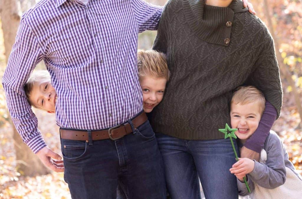 close up of the children of a family peeking out from behind their parents and make silly faces