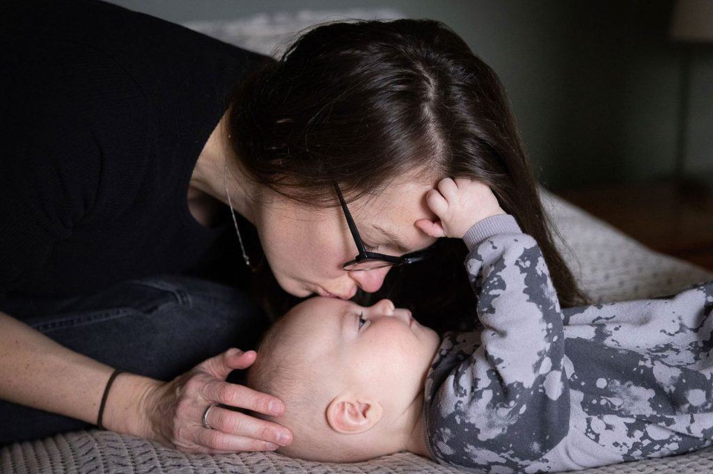 a mom kisses her baby's forehead as the baby reaches for hers