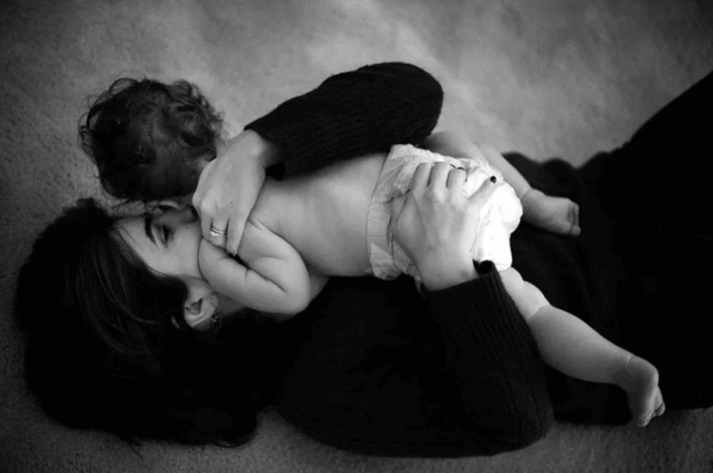 a mom holds a baby in a diaper close to her body as she rolls on the floor