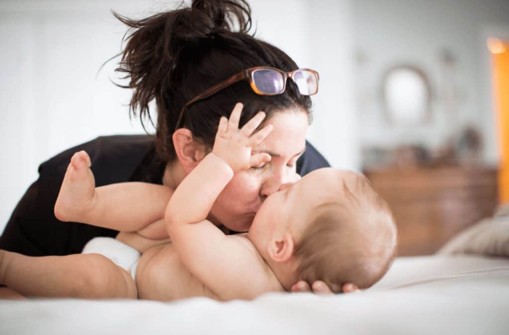 a mom kisses her baby as he reaches for the glasses on her head