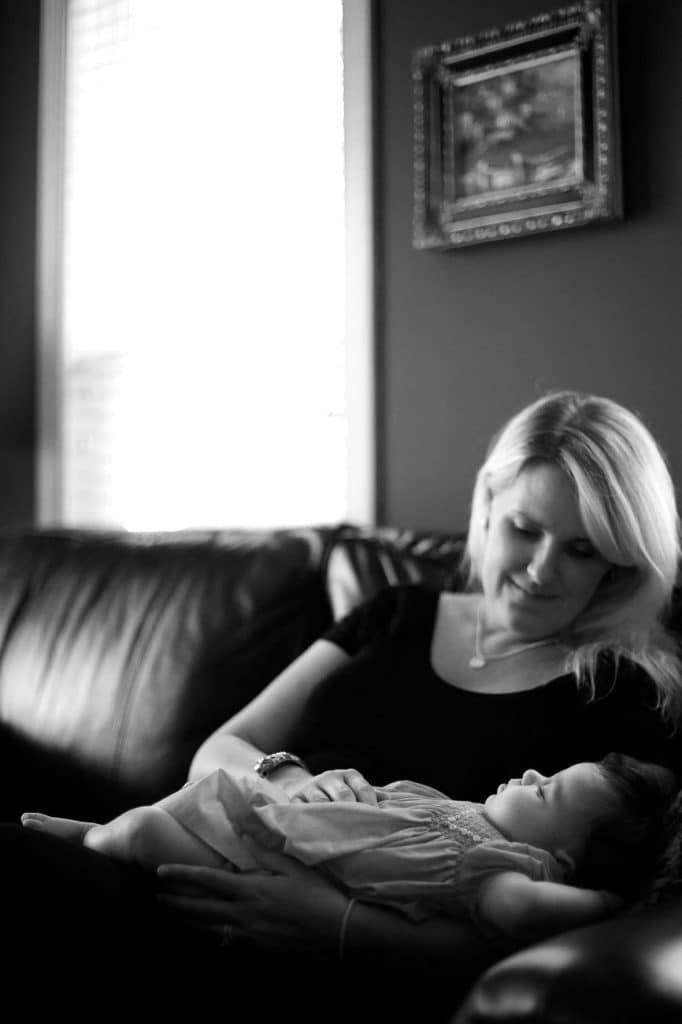 a mom stares at her baby as she naps in her arms