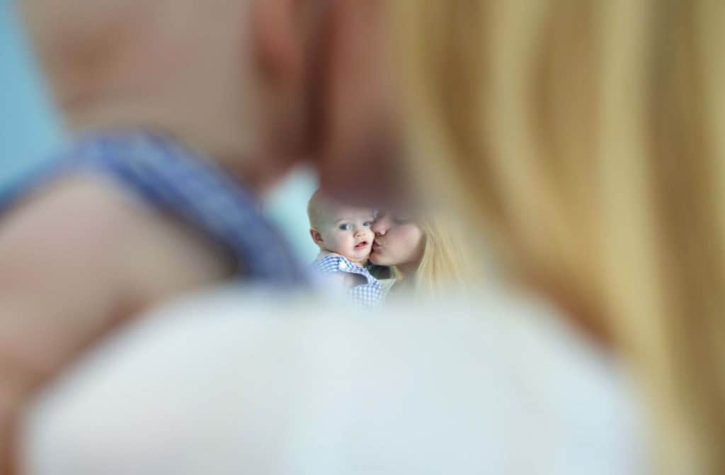 the mirror reflection of a mom cuddling her baby is visible through a tiny gap between their head and shoulders