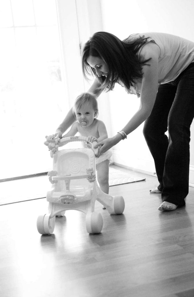 a mom helps her baby use a walking toy to stand