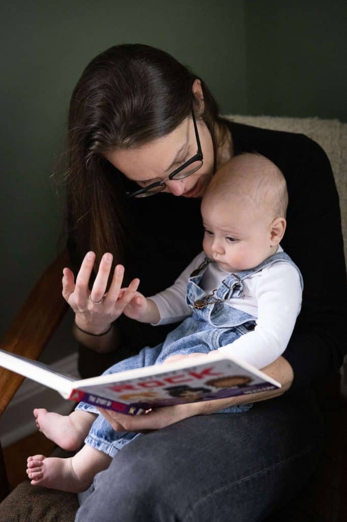 a mom reads to her baby and holds his hand in hers